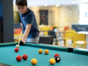 a man playing pool with balls on a pool table at Ibis Styles Cognac in Châteaubernard