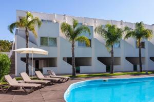 a hotel with a swimming pool and chairs and palm trees at Lagoa Hotel in Lagoa
