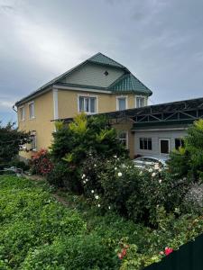 a yellow house with a green roof and some flowers at Nazik Guest House in Barskoon