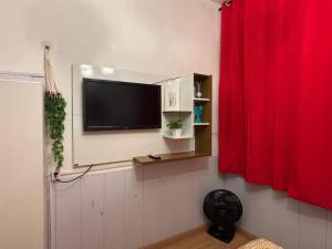 a television on a wall with a red curtain at Apartamento para duas pessoas com cama de casal in Teresópolis