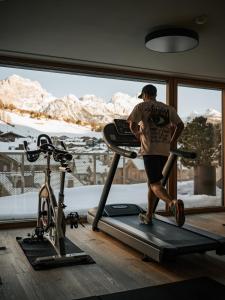 a man on a treadmill in a gym with a view of mountains at Hotel Tofana in San Cassiano