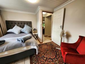 a bedroom with a bed and a red chair at Hogsback Misty Oaks Cottage in Hogsback