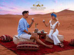 a man and a woman sitting in the desert holding drinks at Desert Luxury Camp & Resort Jaisalmer in Jaisalmer