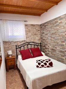 a bedroom with a bed with red pillows and a brick wall at Chalet Rutas de Valsequillo in Valsequillo