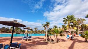 a pool with chairs and umbrellas and palm trees at NEW CASA BLU - Oasis Tamarindo 1 in Corralejo