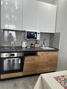 a kitchen with white cabinets and a stove and a sink at Dostar Apartments in Karagandy