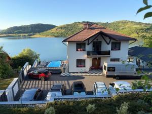 a house with cars parked in a parking lot next to a lake at Panorama Lake Resort in Bezidu Nou