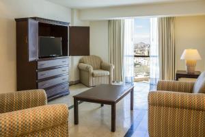 a living room with a tv and chairs and a table at Fiesta Inn Ciudad Juarez in Ciudad Juárez