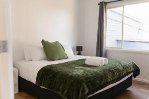 a bedroom with a bed with a green blanket and a window at Hamptons on the Bay in Swansea