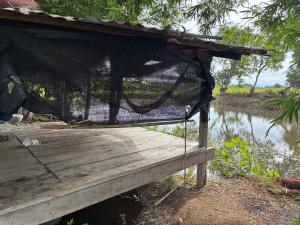 a hammock on a wooden deck next to a river at The Sawmill Lakeside Hut in Ban Nong Sakae