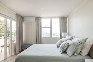 a white bedroom with a large bed with pillows at Stunning Beachfront penthouse-Beach District Views in Sydney