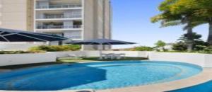 a blue swimming pool with an umbrella and a building at Dalgety 104 in Townsville