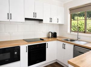 a kitchen with white cabinets and a black dishwasher at Springview Cottage- captivating bush retreat in Hepburn Springs