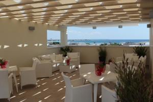 een restaurant met witte tafels en witte stoelen en de oceaan bij Hotel Perla Dello Ionio in Torre Lapillo
