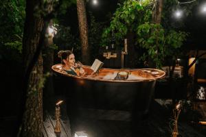 a woman reading a book in a bathtub in a forest at Feelmore Tiny House Karancsalja in Karancsalja