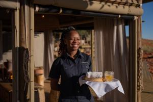a woman holding a tray of bread and orange juice at Wolwedans Dune Camp in NamibRand