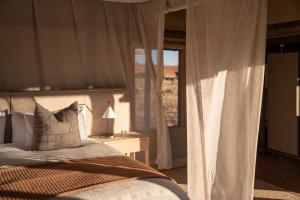 a bedroom with a bed and a window with curtains at Wolwedans Desert lodge in NamibRand +16 photos