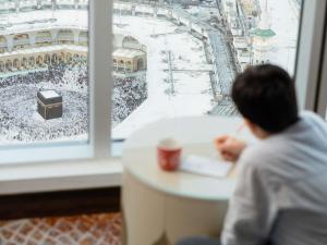 a man sitting at a table looking out of a window at a concert at Swissotel Makkah in Mecca