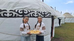 two girls holding a plate of food in front of a tent at Kambar-ata yurt camp in Song-Kul