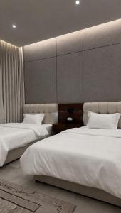 two beds in a hotel room with white sheets at شقة بغرفتين نوم وصالة in Hail