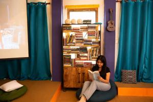 a woman sitting on the floor reading a book at Loopin Mcleodganj in McLeod Ganj