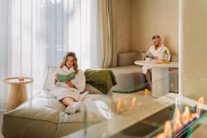 a woman sitting on a couch reading a book in a living room at Luxury Wellness Suite with Jacuzzi & Sauna – Woodz Lodges in Heusden - Zolder +77 photos