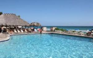 a large blue swimming pool with chairs and the ocean at Ocean Manor Tiki Sunset Retreat in Fort Lauderdale