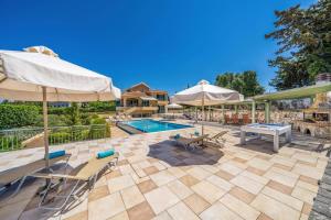 a patio with a pool and tables and umbrellas at Villa Emelisse by Villa Plus in Fiskardo