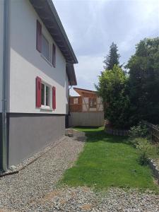 a white house with red windows and a yard at Neues 2 Zimmer Schmuckstück in Ergetsweiler