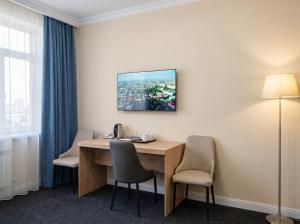 a room with a desk with chairs and a tv on the wall at Avangard Hotel in Almaty