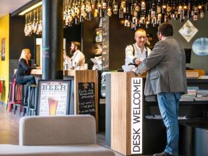 a man standing at a bar talking to a bartender at Novotel Lille Centre Gares in Lille