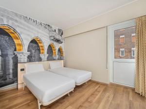 two beds in a room with a wall with arches at B&B Hotel Como City Center in Como
