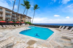 a swimming pool with chairs and the ocean in the background at Sea Village 2106 in Kailua-Kona