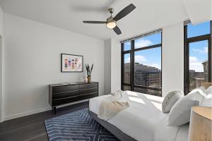 a white bedroom with a ceiling fan and a large window at Placemakr Marymount Ballston in Arlington