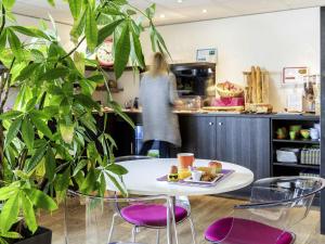 a table with purple chairs and a woman in a kitchen at ibis Styles Rennes St. Gregoire in Saint-Grégoire