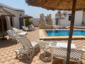 a group of chairs and a swimming pool with an umbrella at Résidence Djerba Oasis in Mezraya