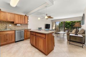 a kitchen with wooden cabinets and a living room at Kihei Akahi D-104 in Wailea