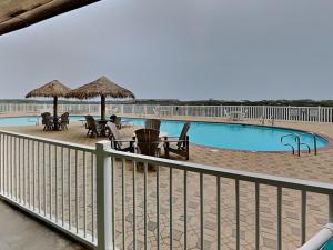 a pool with chairs tables and umbrellas next to a fence at Port A Condo in Port Aransas +9 photos
