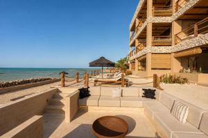a building on the beach with a couch and an umbrella at Luxury Villas By Awa Holbox - Beachfront in Holbox Island