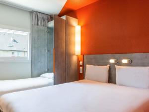 a bedroom with two beds and an orange wall at ibis budget Senlis in Senlis