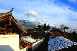 Blick auf schneebedeckte Dächer von Gebäuden und Bergen in der Unterkunft Lijiang Baisha Free Time Designed Hotel in Lijiang