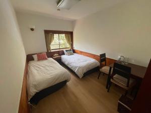 a bedroom with two beds and a desk and a window at Shika Lodge Izu in Ito