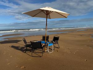 three chairs and an umbrella on a beach at Vila Chalés in Mucuri