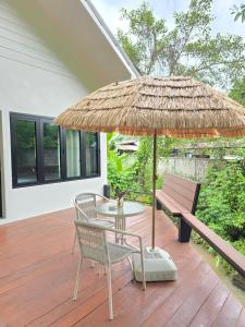 a patio with a table and a straw umbrella and a bench at Mind's Homestay มายด์โฮมสเตย์ in Kampong Huaibū