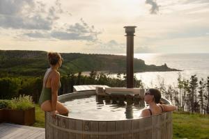two women sitting in a hot tub with the ocean at Birch - Luxury Oceanview Cottage with Hot Tub & Private Beach Access near Cabot Trail in Chimney Corner