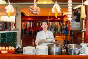 a chef standing behind a counter holding a bowl of food at Victoria Nui Sam Lodge in Chau Doc