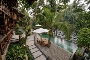an outdoor patio with an umbrella and chairs next to a pool at The Campuhan Retreat in Munggu
