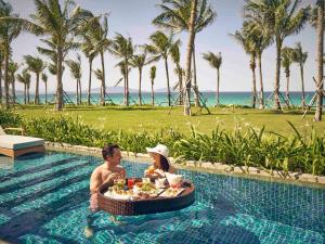a man and woman sitting in a pool at a resort at Mövenpick Resort Cam Ranh in Cam Ranh