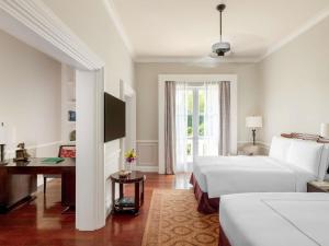 a bedroom with two beds and a desk and a window at Raffles Grand Hotel d'Angkor in Siem Reap