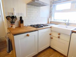 a white kitchen with a sink and a stove at Ferndene Cottage in Hinderwell